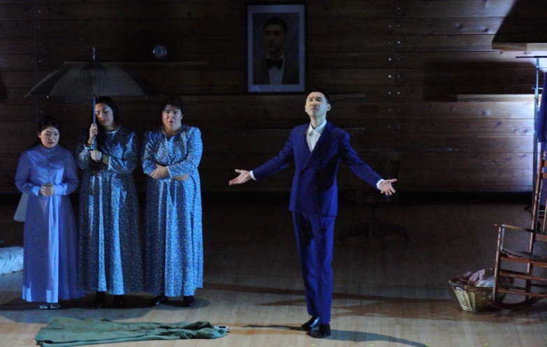 A person in a blue suit standing on a stage with two women in the background

Description automatically generated