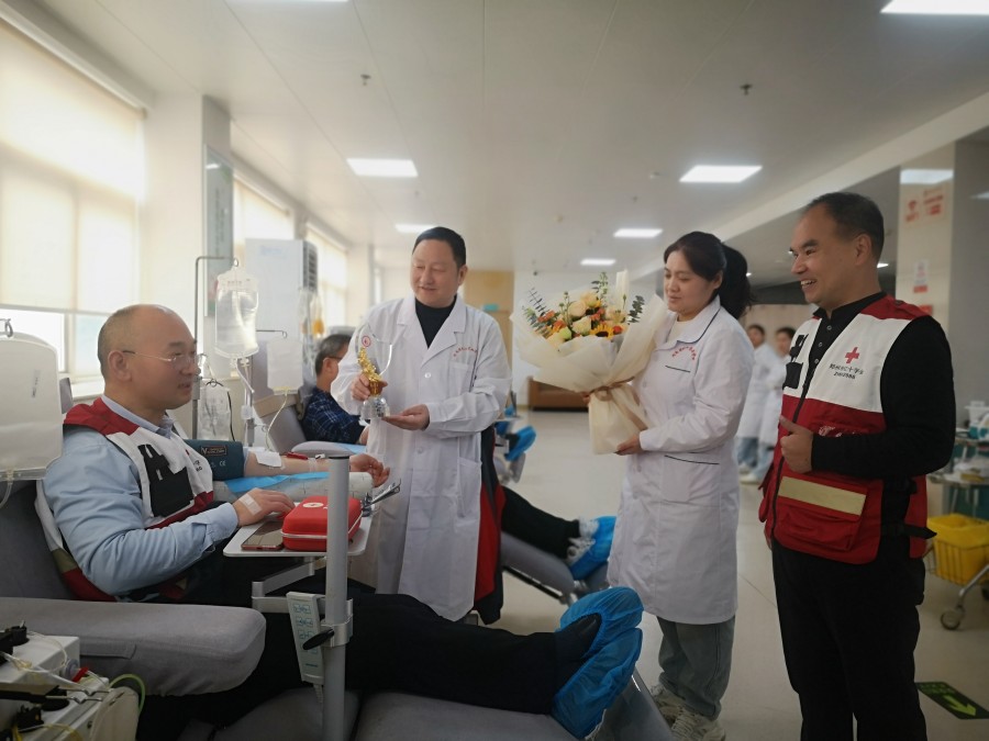 河南省红十字血液中心工作人员为王晓送上鲜花和“无偿献血三百次”奖杯.jpg